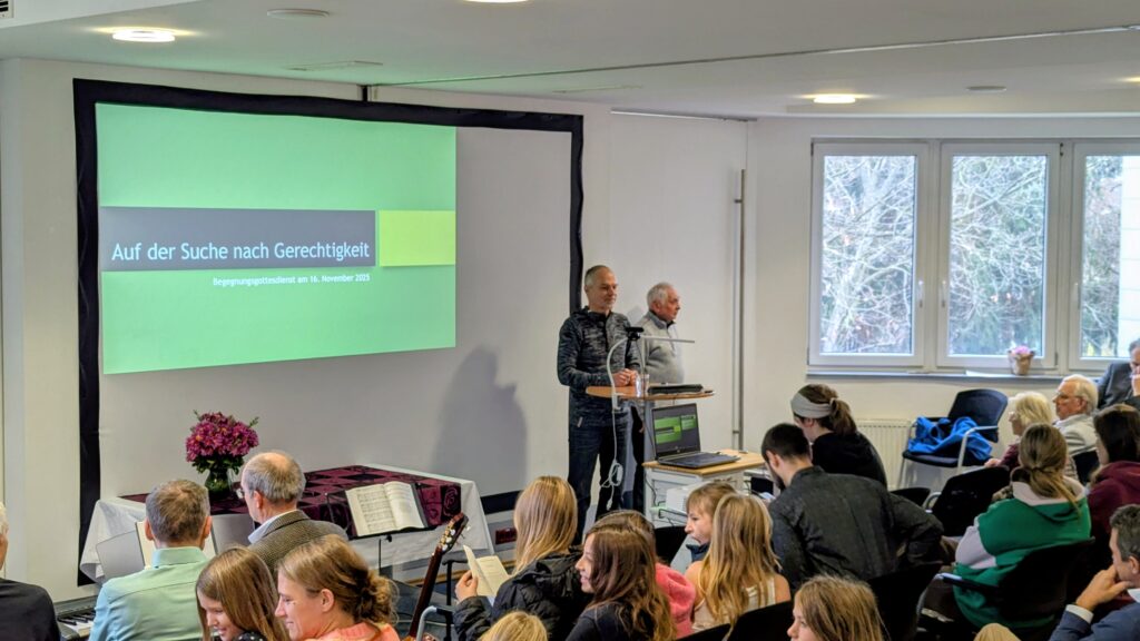 Foto von einem Begegnungsgottesdienst, Halbtotale vom Raum, sichtbar sind der Sprecher und Gäste in der Versammlung